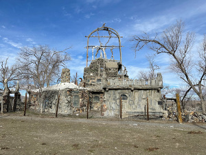 The monument consists of stones together with a miscellany of discarded objects found in the nearby desert, all held together with concrete.  Glass items are placed in the walls in order to allow some light to pass within the building.  It has been surrounded by a tall wire security fence.
