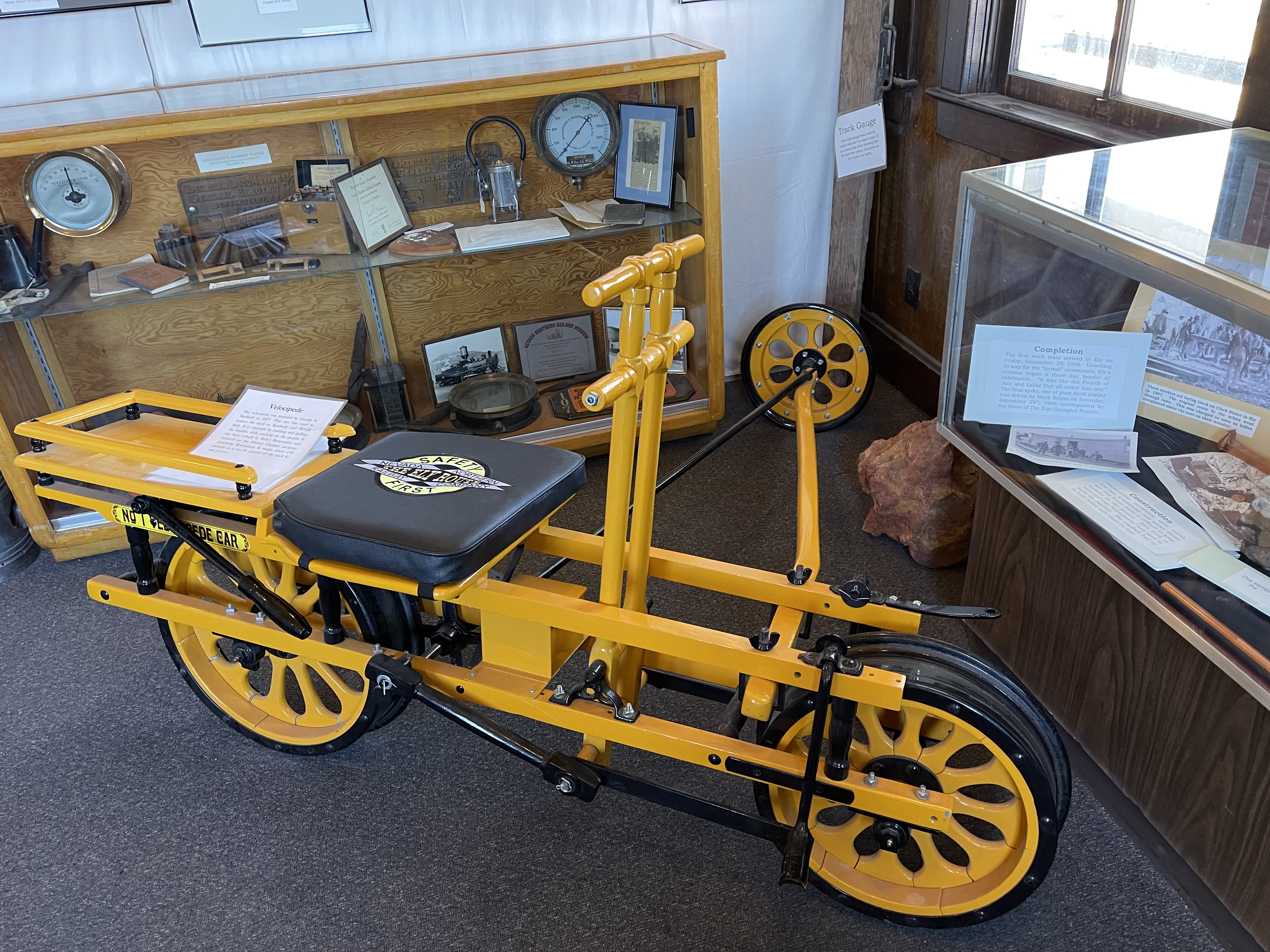with a black leather seat and brilliant yellow frame and wheels, the cart sits on the museum floor, with the third wheel extending for balance on the second rail.  Power is supplied by a hand bar.